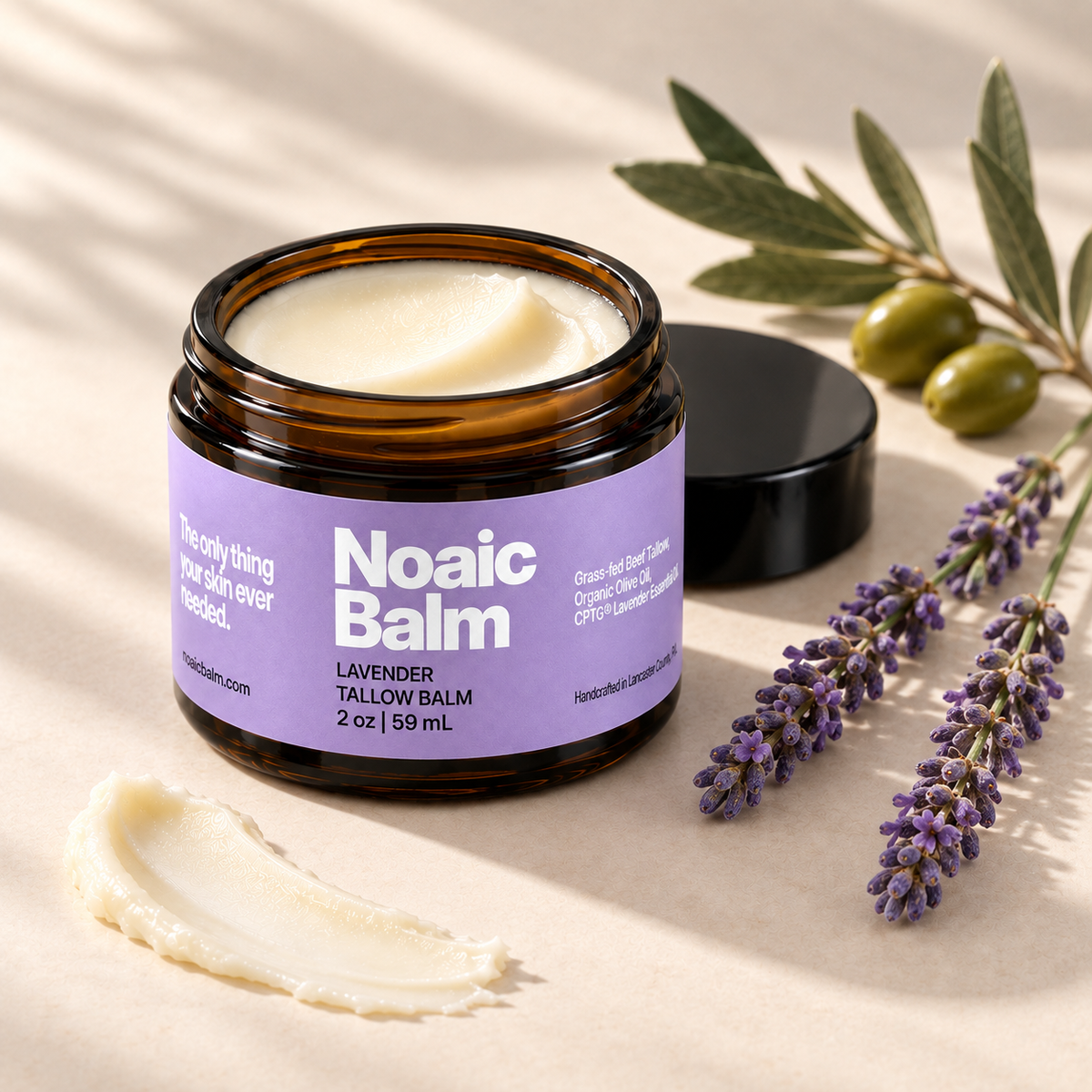 Open Noaic Lavender tallow balm jar with lavender stems, olives and a small swipe of balm.